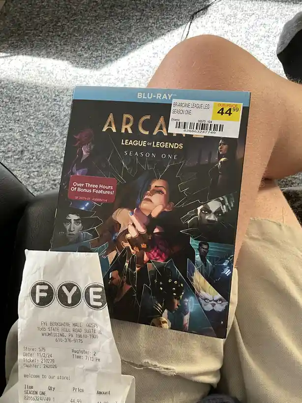 A person holds a 'League of Legends: Arcane Season One' Blu-ray case with a yellow price sticker reading 'OUR PRICE 44.99'…
