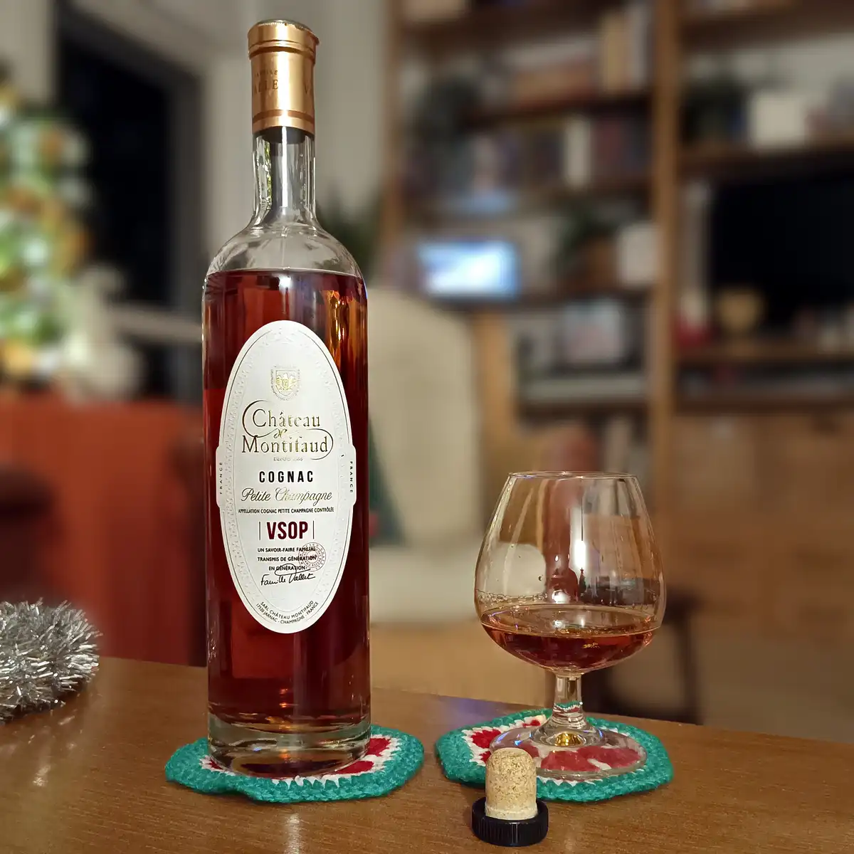 A bottle of Château de Montifaud VSOP Cognac Petite Champagne sits on a wooden table next to a snifter glass partially…