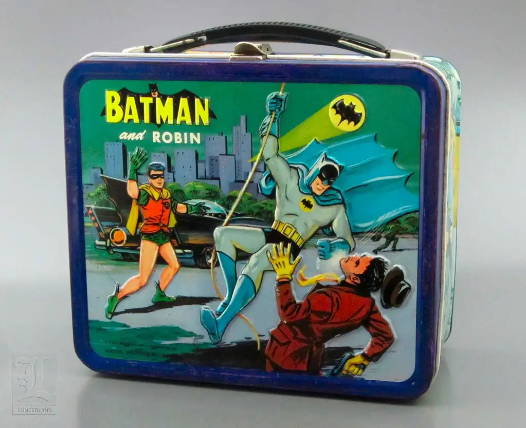 A vintage Batman and Robin lunchbox features a classic comic book illustration of Batman swinging on a rope while Robin runs…