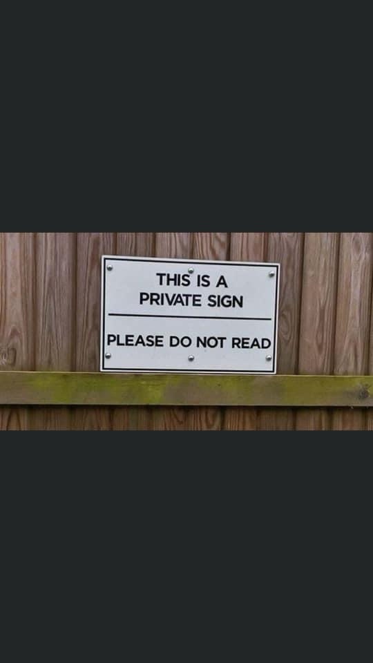 A white rectangular sign with black text is mounted on a wooden fence. The sign reads 'THIS IS A PRIVATE SIGN' on the top…