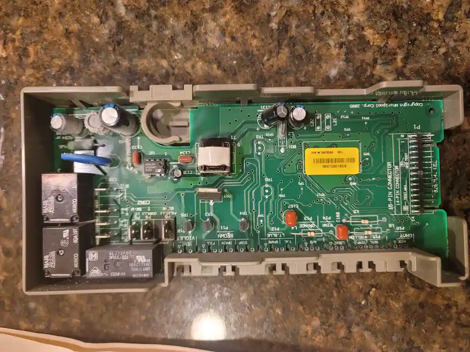 A close-up photo of a green circuit board from a Whirlpool washing machine control panel, showing various electronic…