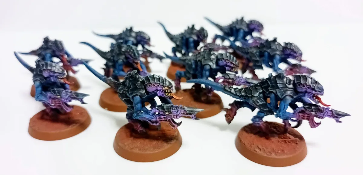 A collection of painted miniature figurines, resembling reptilian or dinosaur-like creatures with dark blue and purple…
