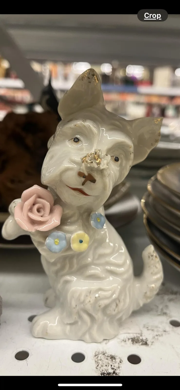 A white ceramic cat figurine, holding a pink rose and adorned with small colorful flowers, has visible damage to its nose…