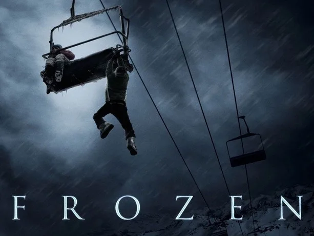 A person is hanging from a broken ski lift chair against a dark, stormy sky with snow falling. The word 'FROZEN' is…