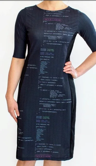 A woman wearing a black dress printed with colorful lines of computer code, standing with one hand on her hip against a…