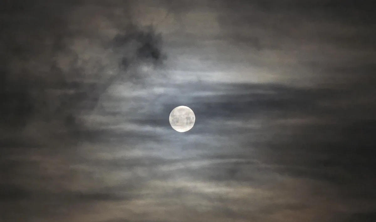 A full moon is visible through a cloudy night sky, with dark and light gray clouds swirling around it. The overlaid text…