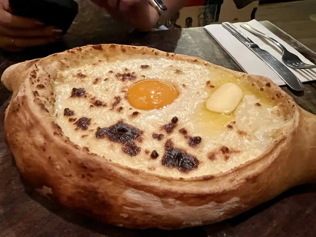 a close-up photo of a baked dish resembling a bread bowl filled with melted cheese, topped with a single raw egg yolk and a…