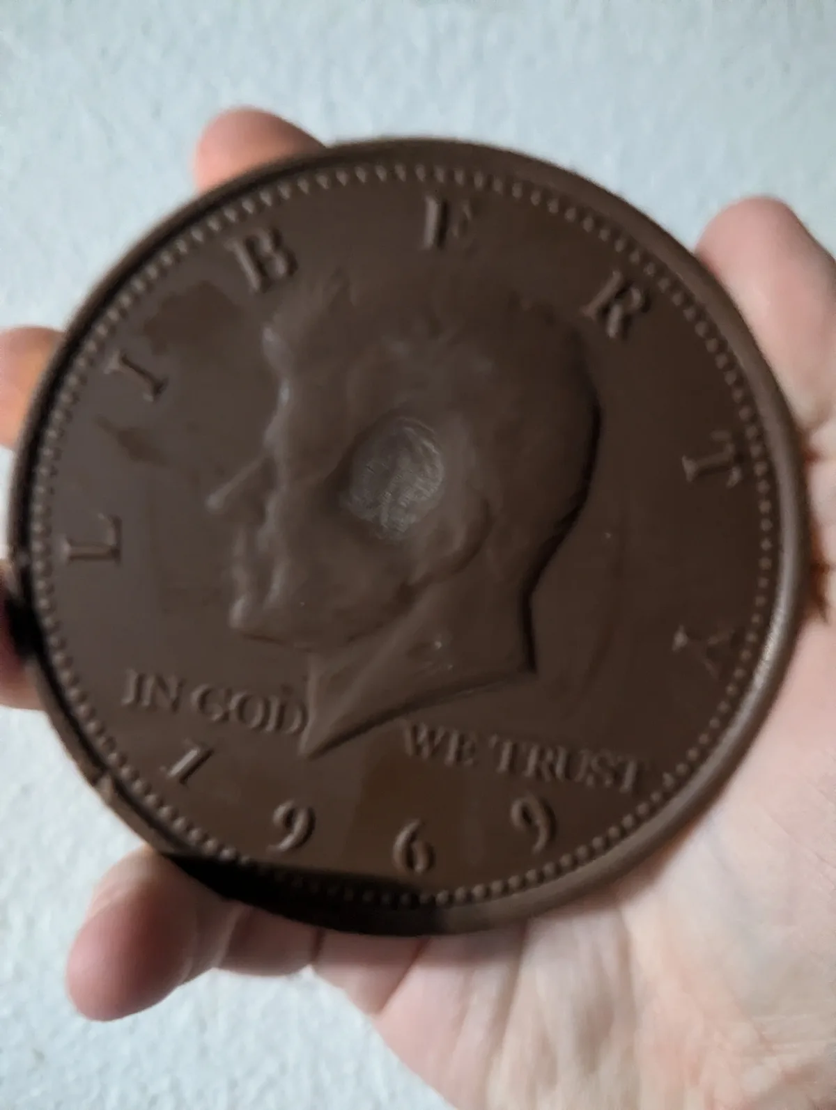 A hand holds a large, chocolate-brown, coin-shaped object resembling a U.S. coin with a profile of Abraham Lincoln, the…