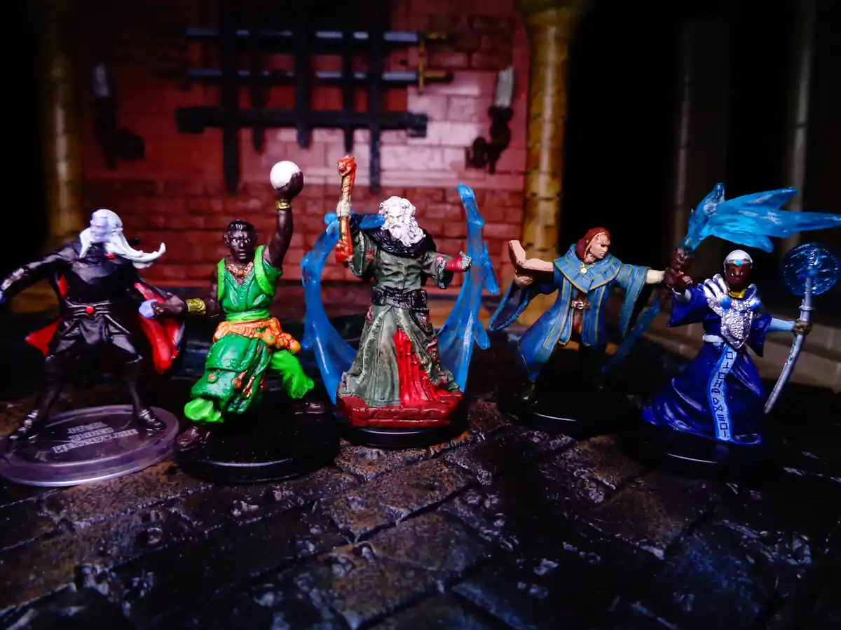 Five painted fantasy miniatures of diverse characters, including a wizard with a staff and blue energy, a cleric with a…