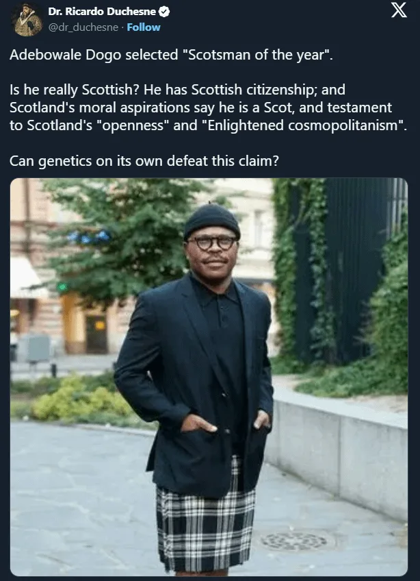 A man wearing a black blazer, glasses, and a plaid kilt stands with hands in pockets. Overlaid text questions if he is truly…