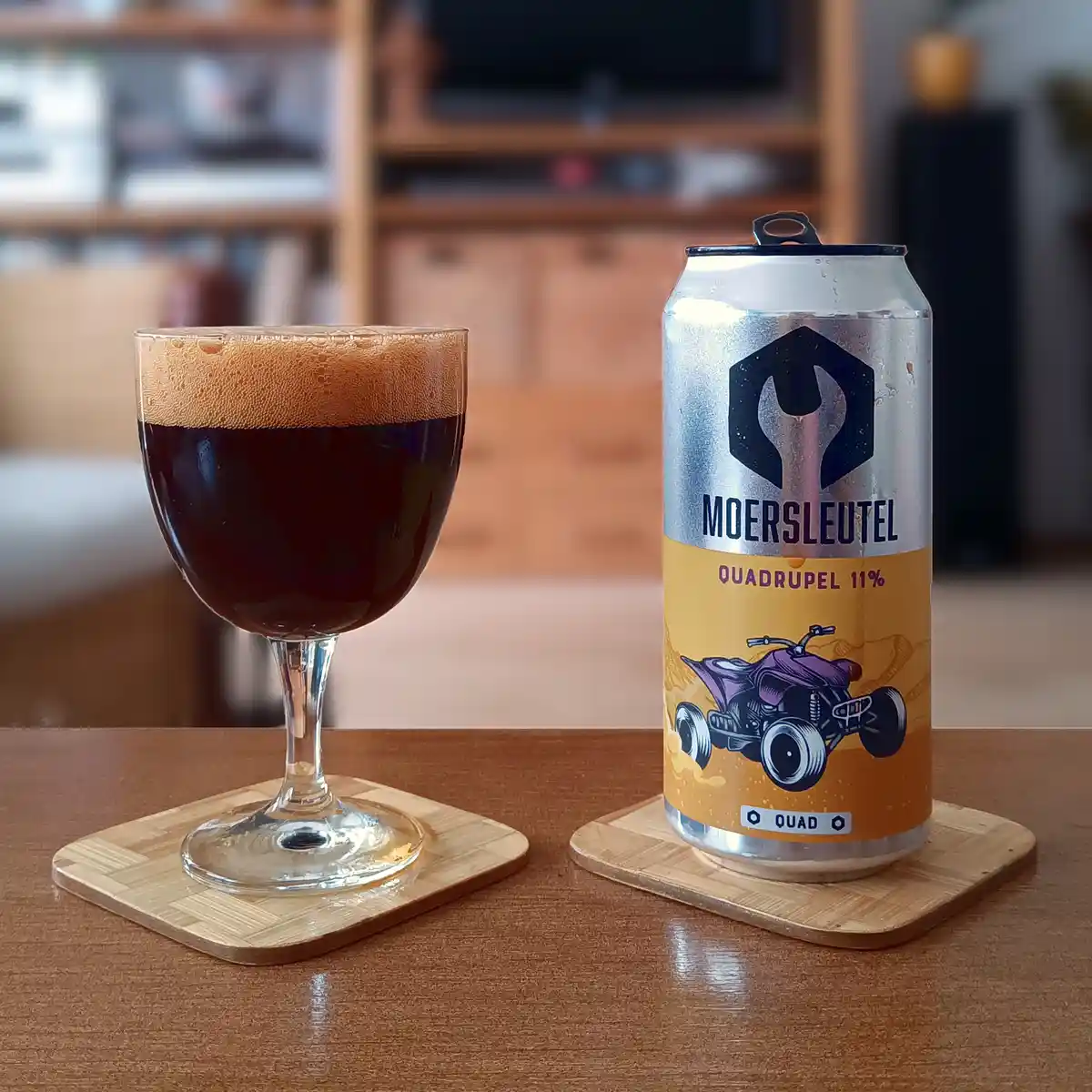 A silver beer can labeled 'MOERSLEUTEL QUADRUPEL 11%' with a purple ATV graphic sits next to a glass of dark beer with a tan…
