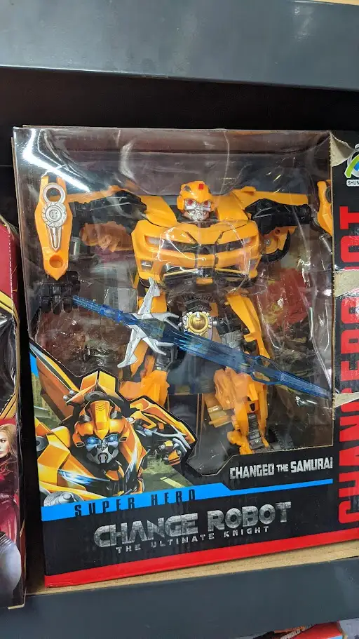 A toy package for a yellow and black robot action figure, resembling Bumblebee from Transformers, is shown in its clear…
