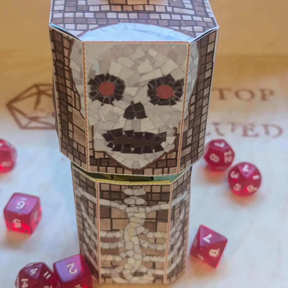 A handmade paper model of a skeleton tower with a mosaic skull face and red eyes, surrounded by translucent red polyhedral…