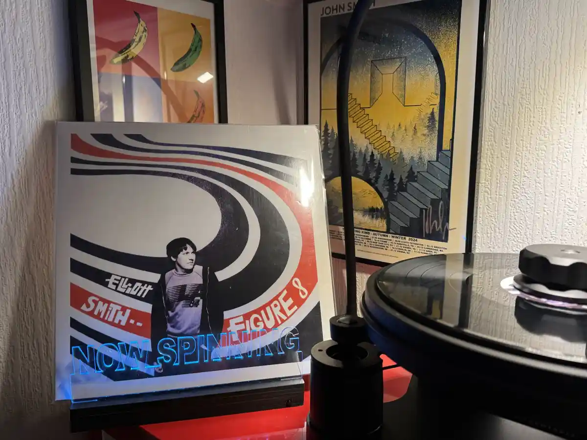 A vinyl record player with a record on it sits next to a glowing acrylic display of the album cover for Elliott Smith's…