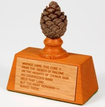A wooden award trophy topped with a pinecone, featuring an engraved plaque with a poem about the Gallipoli campaign. The…