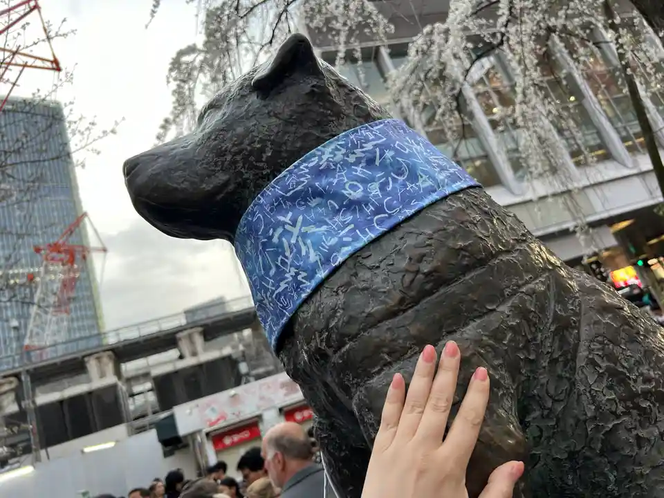 A close-up photo shows a person's hand gently resting on the back of a large bronze statue of a dog, which is wearing a blue…
