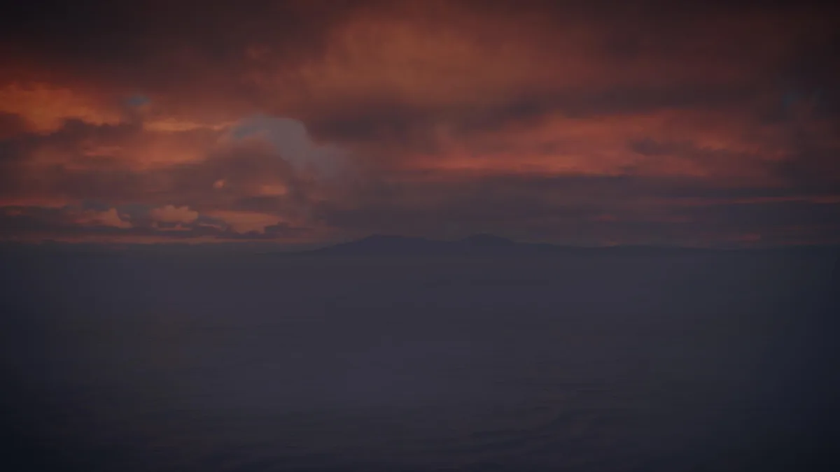 A moody, atmospheric image of a dark ocean under a dramatic, fiery orange and red sunset sky with distant mountain…