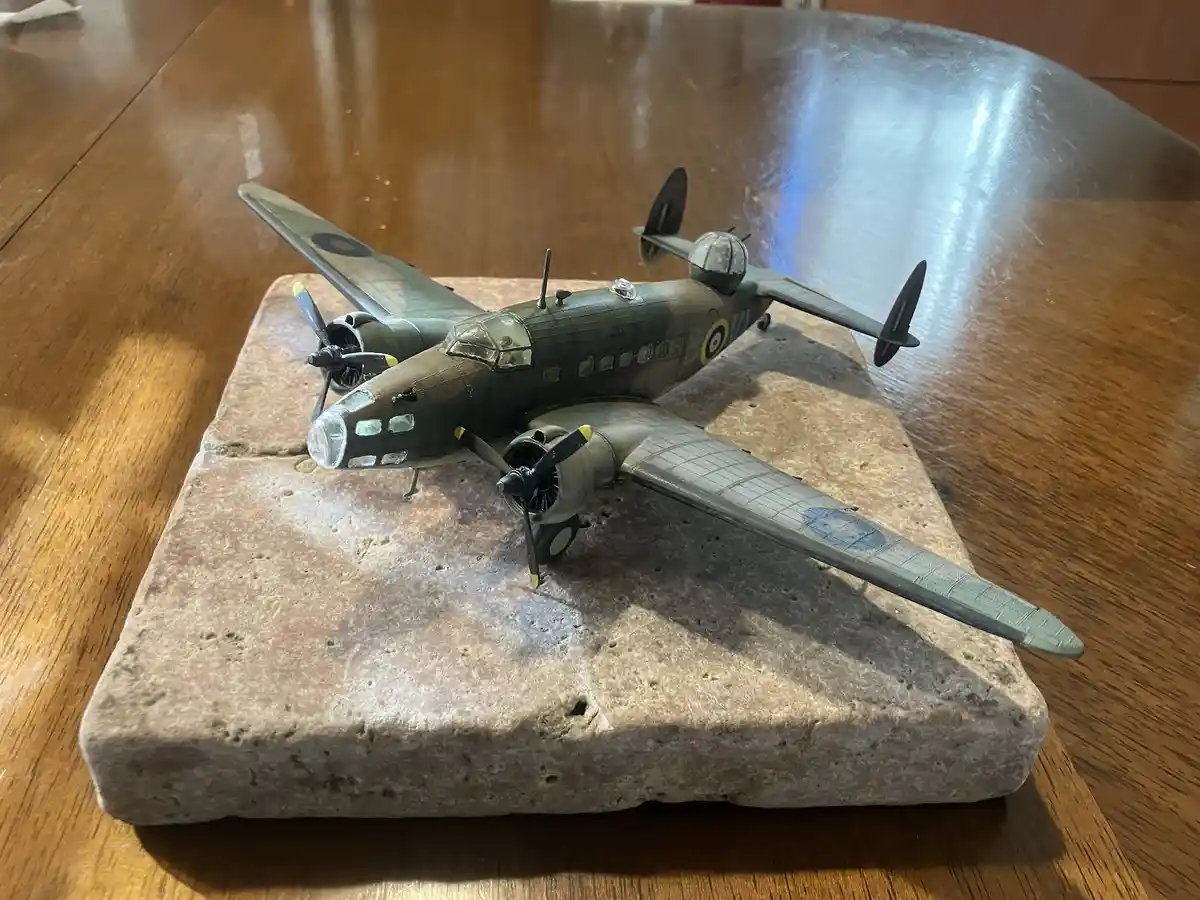 A detailed model of a green military aircraft with roundels is displayed on a rough, porous stone block that resembles a…