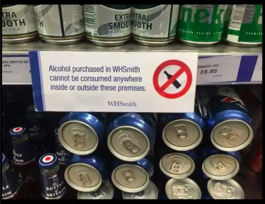 A photo of a WHSmith alcohol shelf with a sign stating 'Alcohol purchased in WHSmith cannot be consumed anywhere inside or…