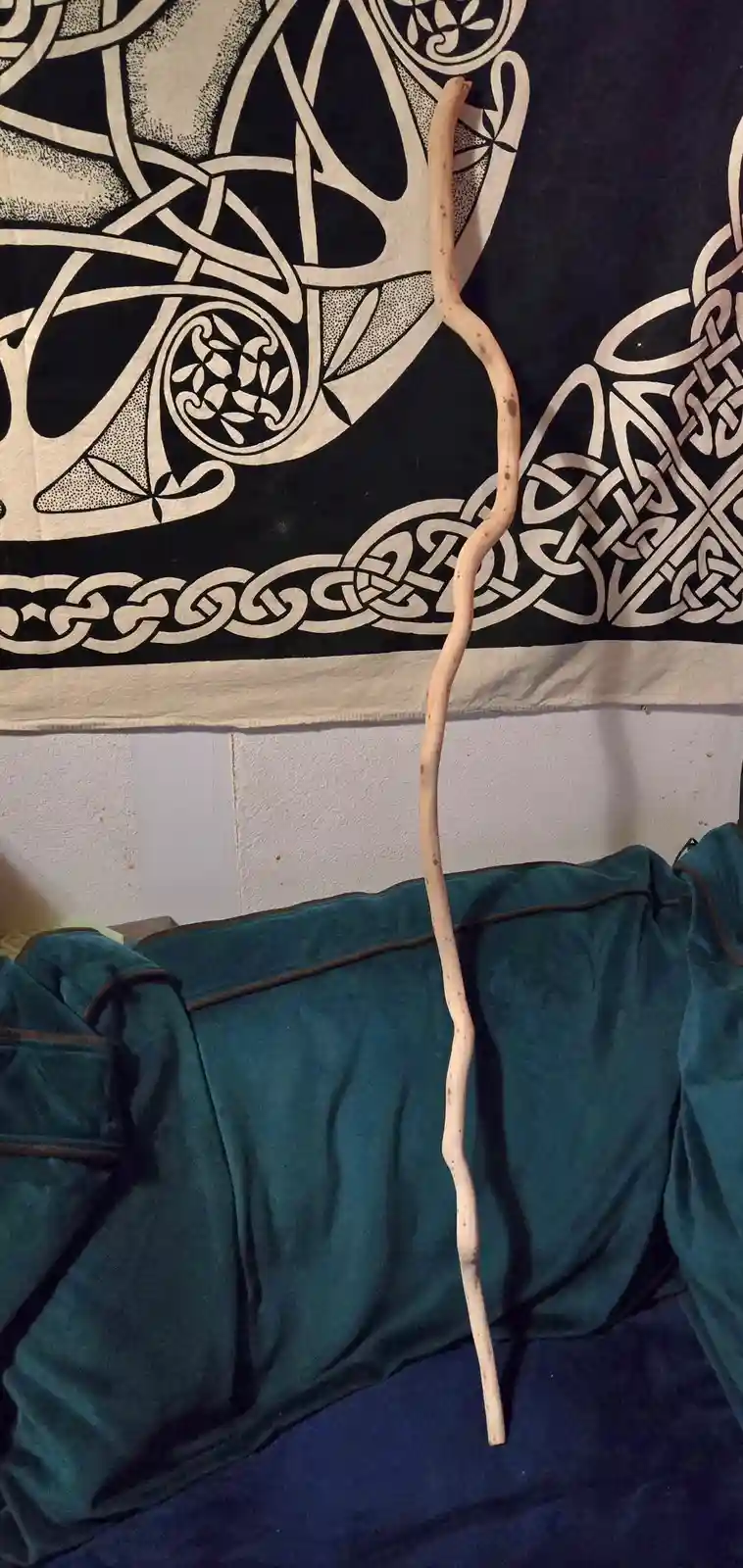 A natural, light-colored, irregularly curved wooden stick, resembling a staff, is propped vertically against a wall behind a…