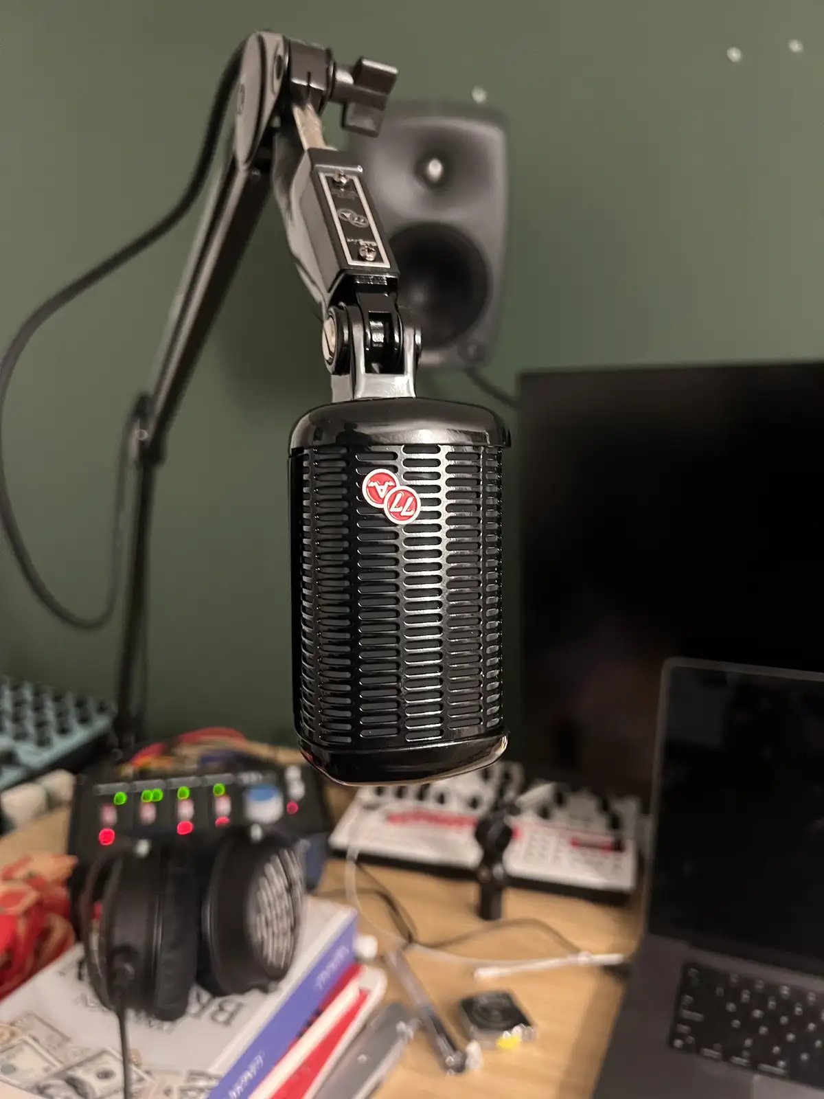 A close-up photo of a black vintage-style condenser microphone on a boom arm, positioned over a cluttered desk with…
