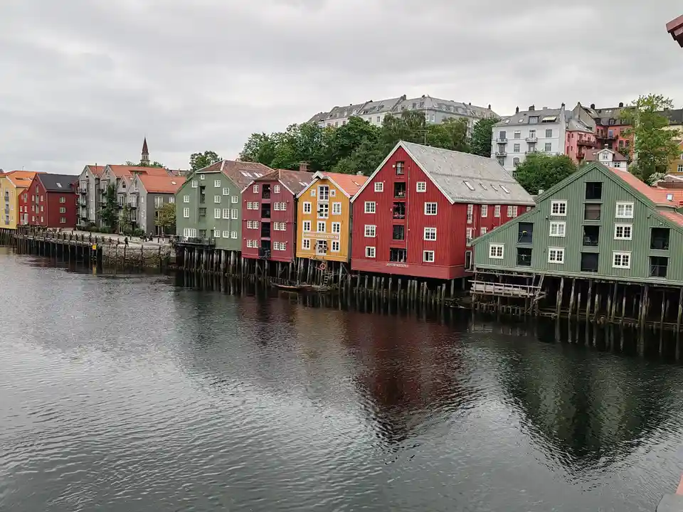 A row of colorful, traditional wooden buildings on stilts along a waterfront under an overcast sky. The buildings are…