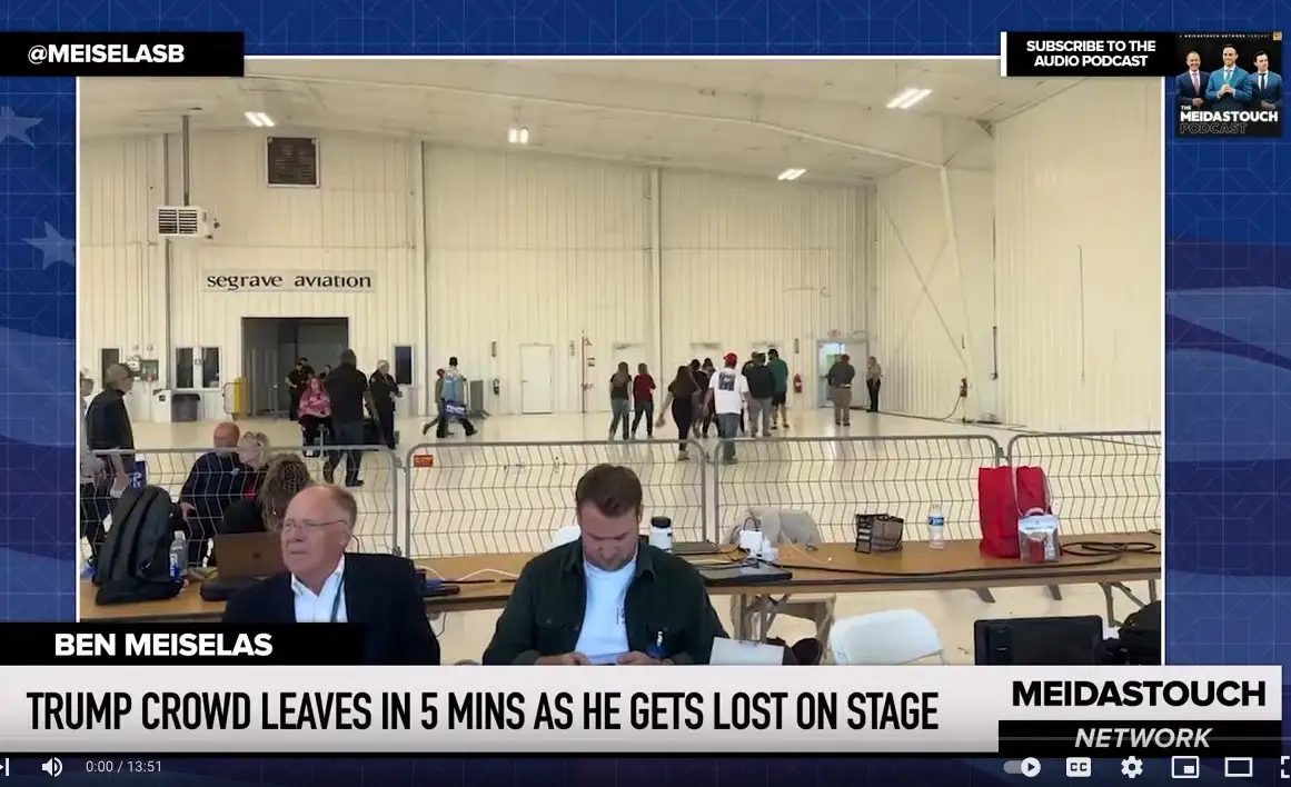 A video screenshot from a news broadcast shows two men seated at a table in front of a large hangar labeled 'segrave…