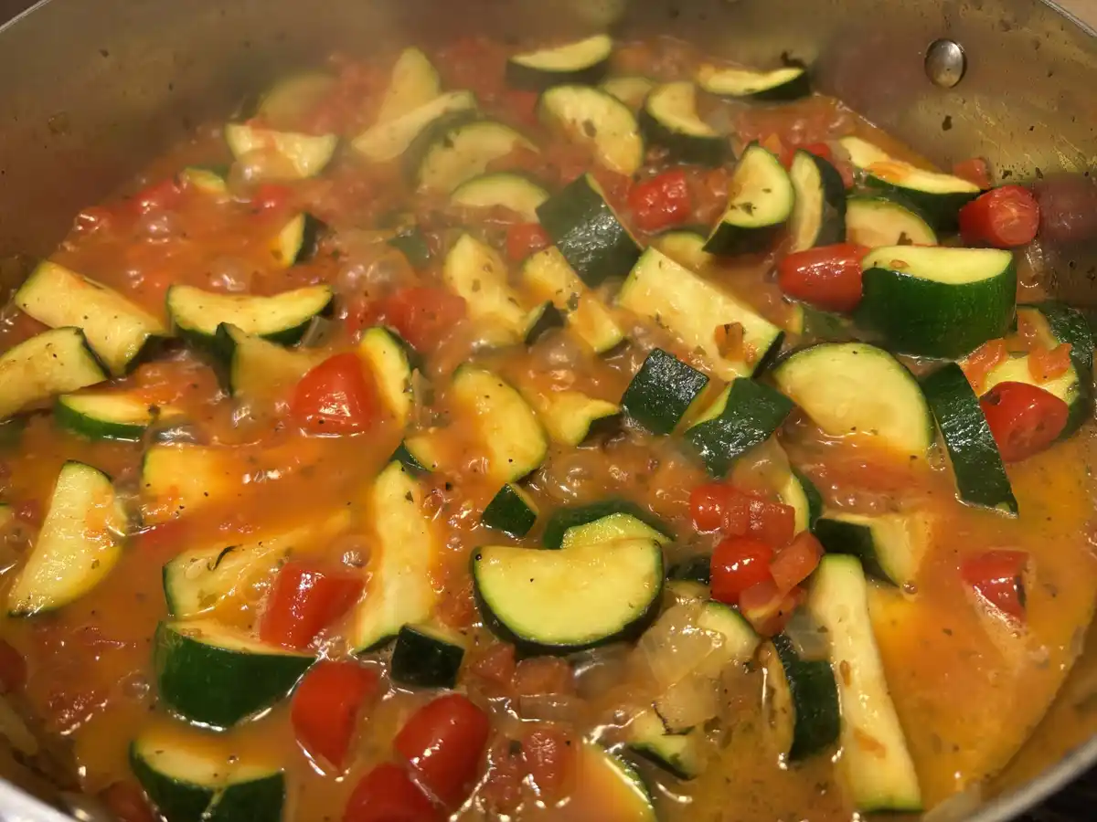 A close-up photo of a bubbling pot of tomato sauce with sliced zucchini and cherry tomatoes, with the text 'zucchini is the…