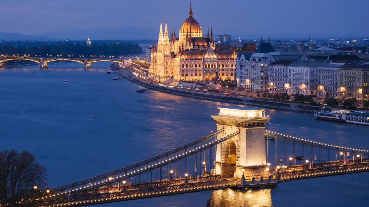 The blue Danube River, a 1,700-mile course, shines at blue hour in Budapest. The Hungarian Parliament Building glows on the…