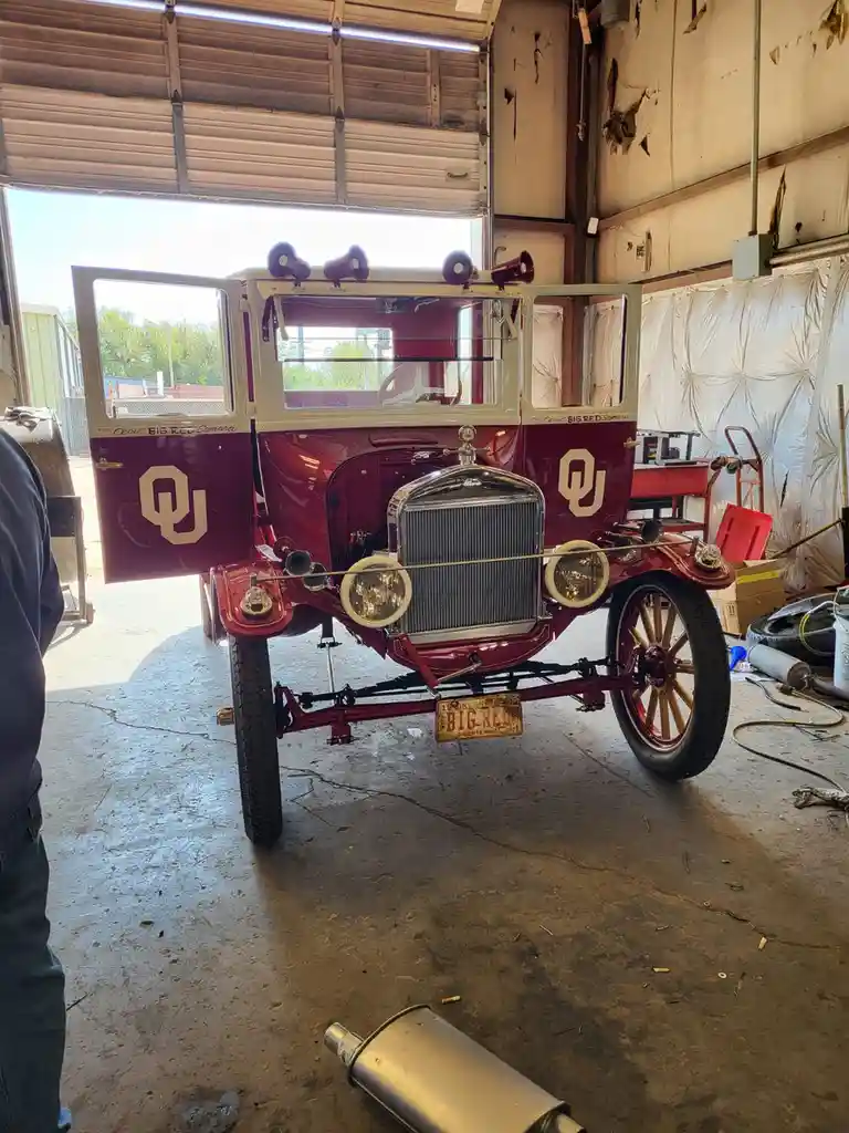 A maroon vintage automobile with 'OU' logos and 'BIG RED' text on its doors and license plate is parked inside a cluttered…