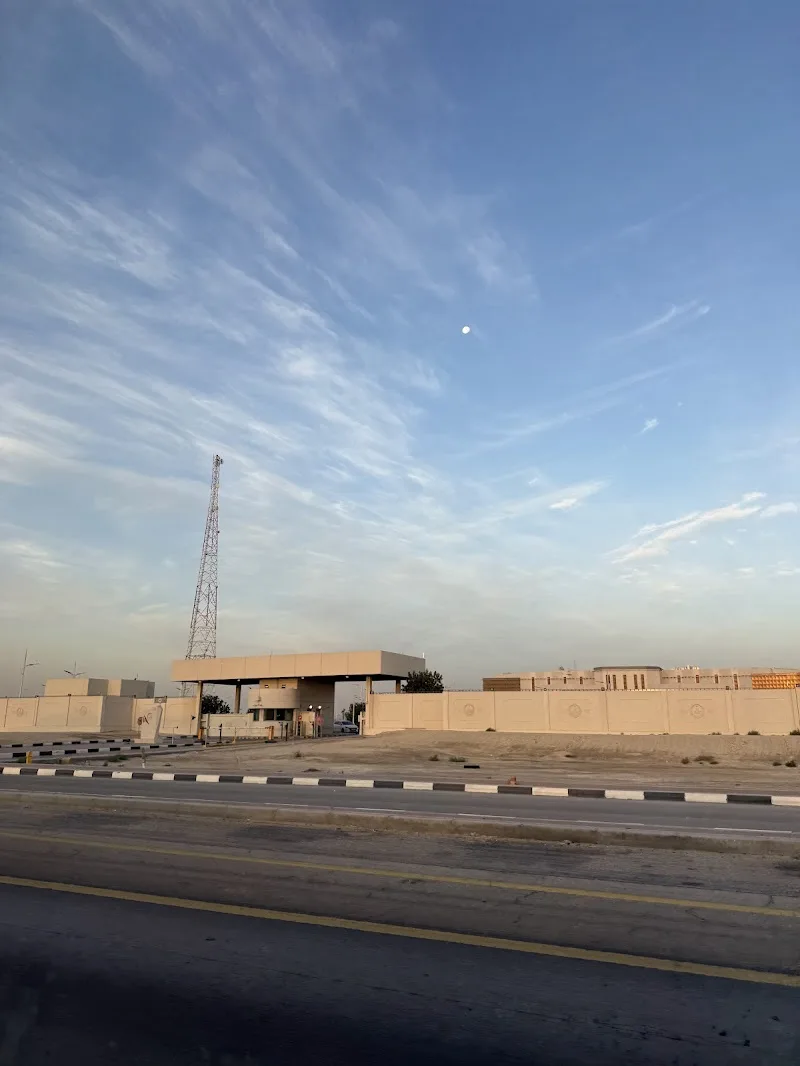 A daytime photo of a desert road with a security checkpoint and a tall radio tower under a blue sky with wispy clouds. A…