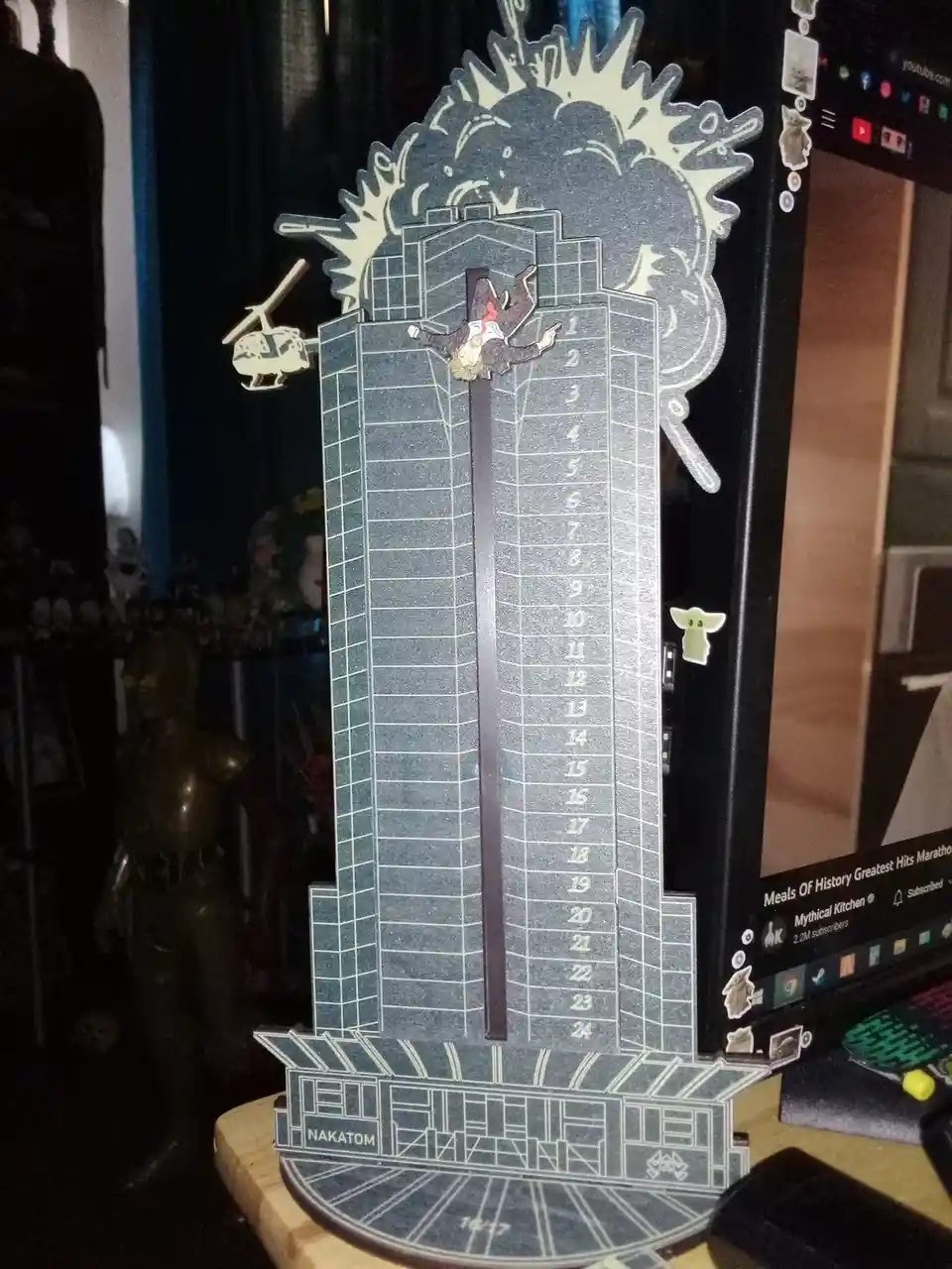 A 3D paper model of the Nakatomi Plaza building from the movie Die Hard, with a miniature figure of John McClane falling…