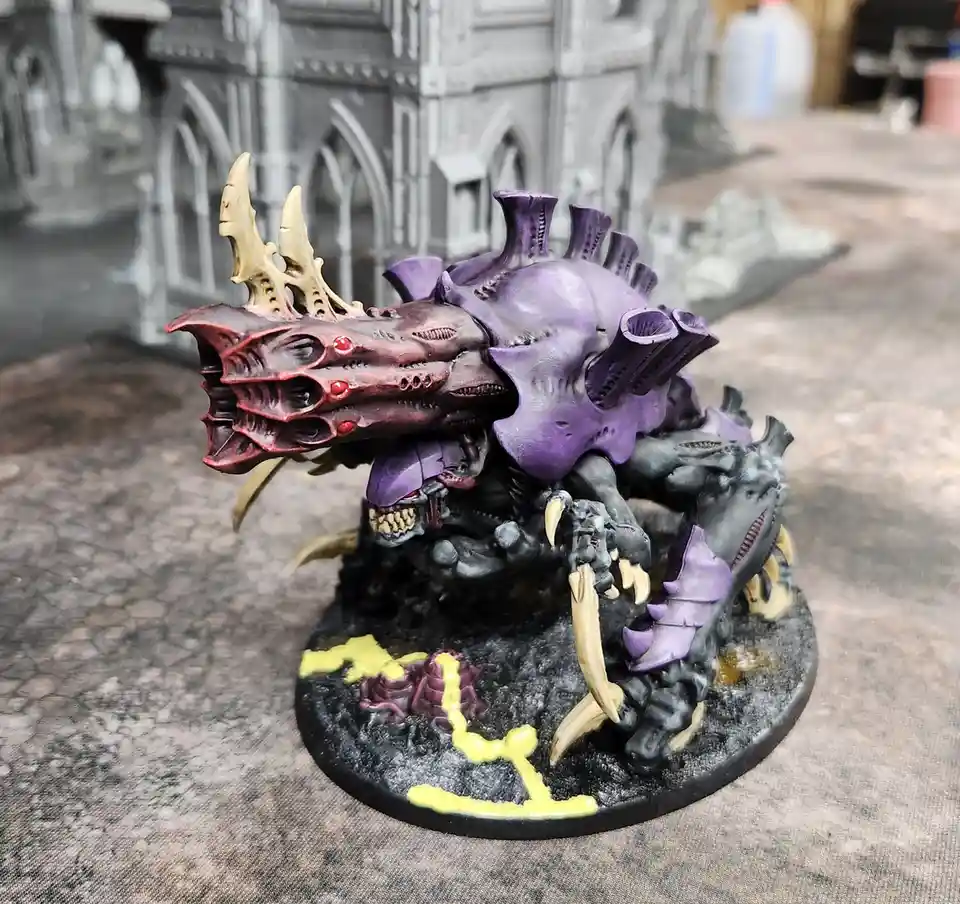 A highly detailed, painted miniature of a monstrous, multi-limbed creature with a purple carapace, red maw, and yellow…