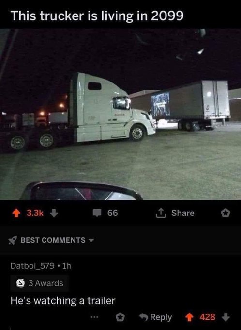 A nighttime photo from inside a car shows a white semi-truck parked in a lot, with its trailer displaying a bright…