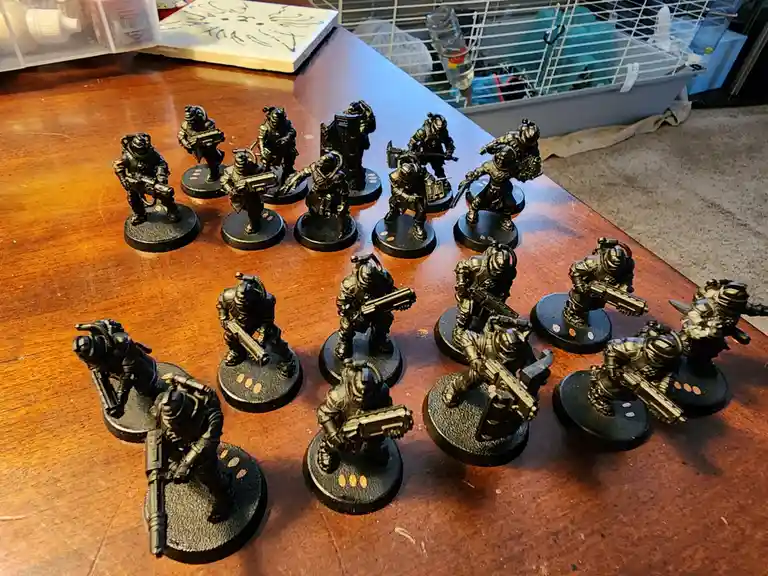 A collection of unpainted, black, futuristic soldier miniatures arranged on a wooden table, each standing on a circular base…