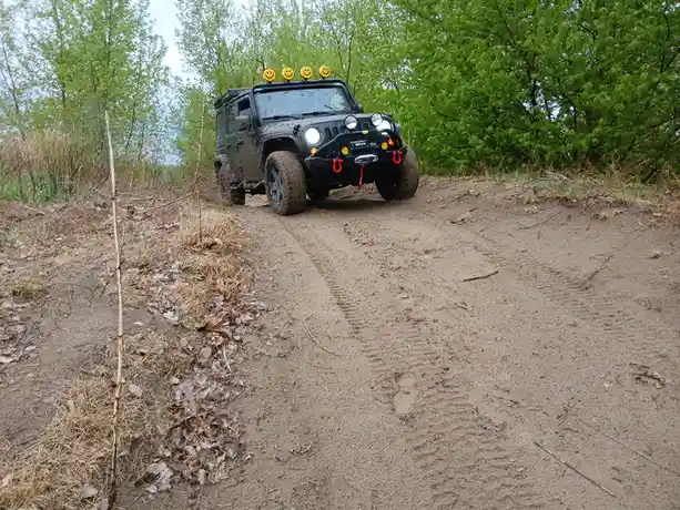 A muddy, off-road Jeep Wrangler with a black bumper, red recovery hooks, and four yellow smiley-face lights on its roof is…