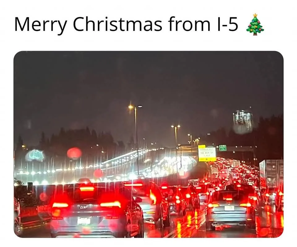 A nighttime photo of a heavily congested highway with cars stopped in traffic, their red taillights glowing in the rain. The…