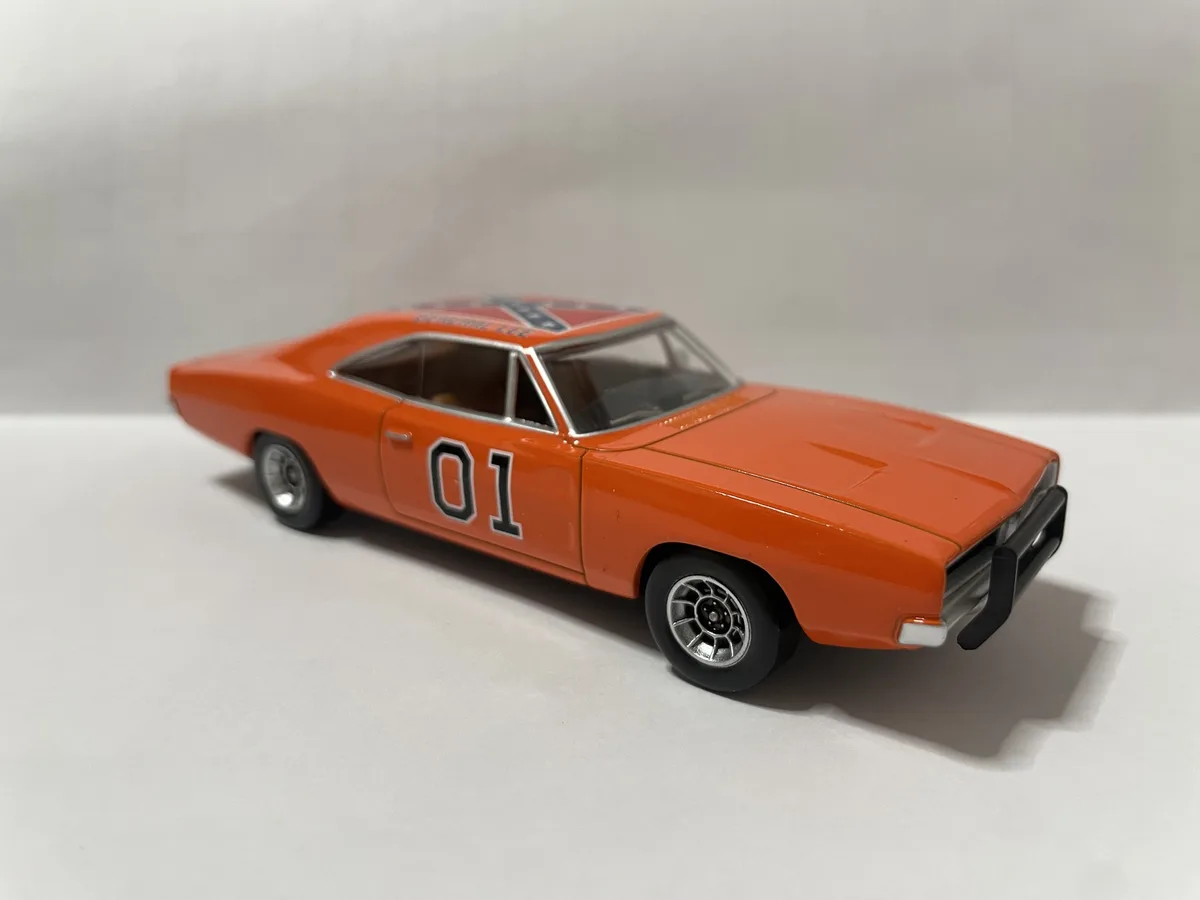 A small orange die-cast model of the iconic Dodge Charger from 'The Dukes of Hazzard' is shown from a three-quarter angle…