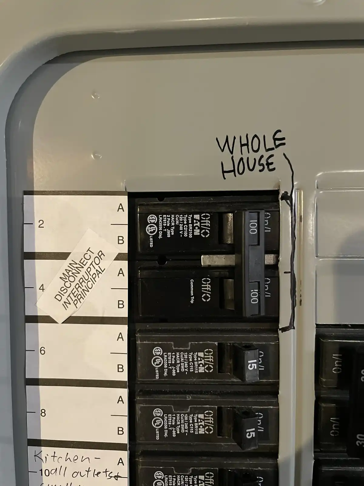 A close-up photo of a residential electrical breaker panel with handwritten labels. The top right corner has 'WHOLE HOUSE'…