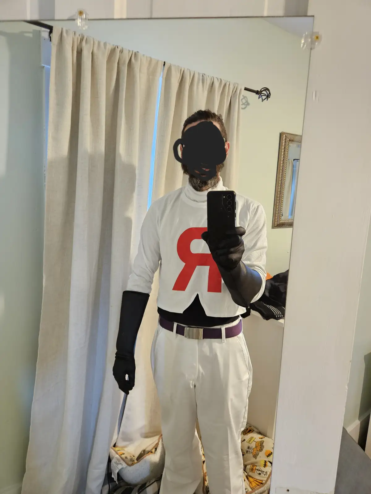A person in a full-body Rocket Team cosplay from Pokémon, featuring a white turtleneck shirt with a large red 'R' logo…