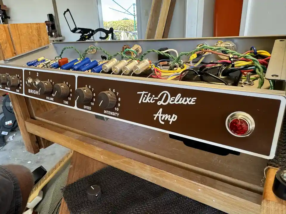 A close-up of a brown guitar amplifier labeled 'Tiki-Deluxe Amp' with knobs for Volume, Tone, Speed, and Intensity. The…