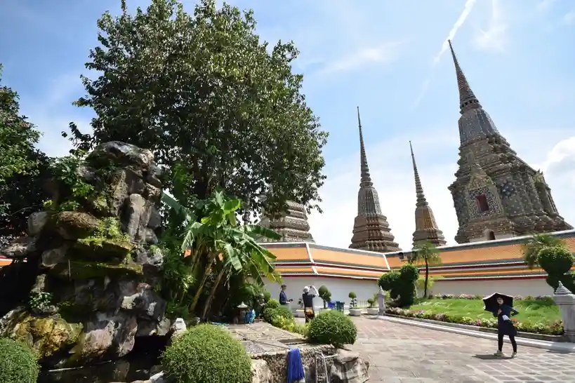 A bright, sunny photo of a temple complex with ornate spires and lush greenery, where a person in dark clothing holds an…