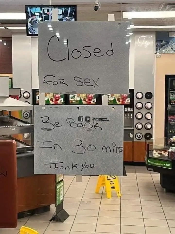 Two gray signs are taped together in a convenience store, humorously announcing 'Closed For Sex' and 'Be Back In 30 min…