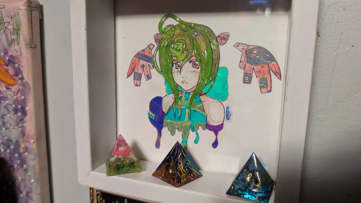 A framed artwork depicts a stylized anime girl with green hair and colorful, dripping paint effects, flanked by two…