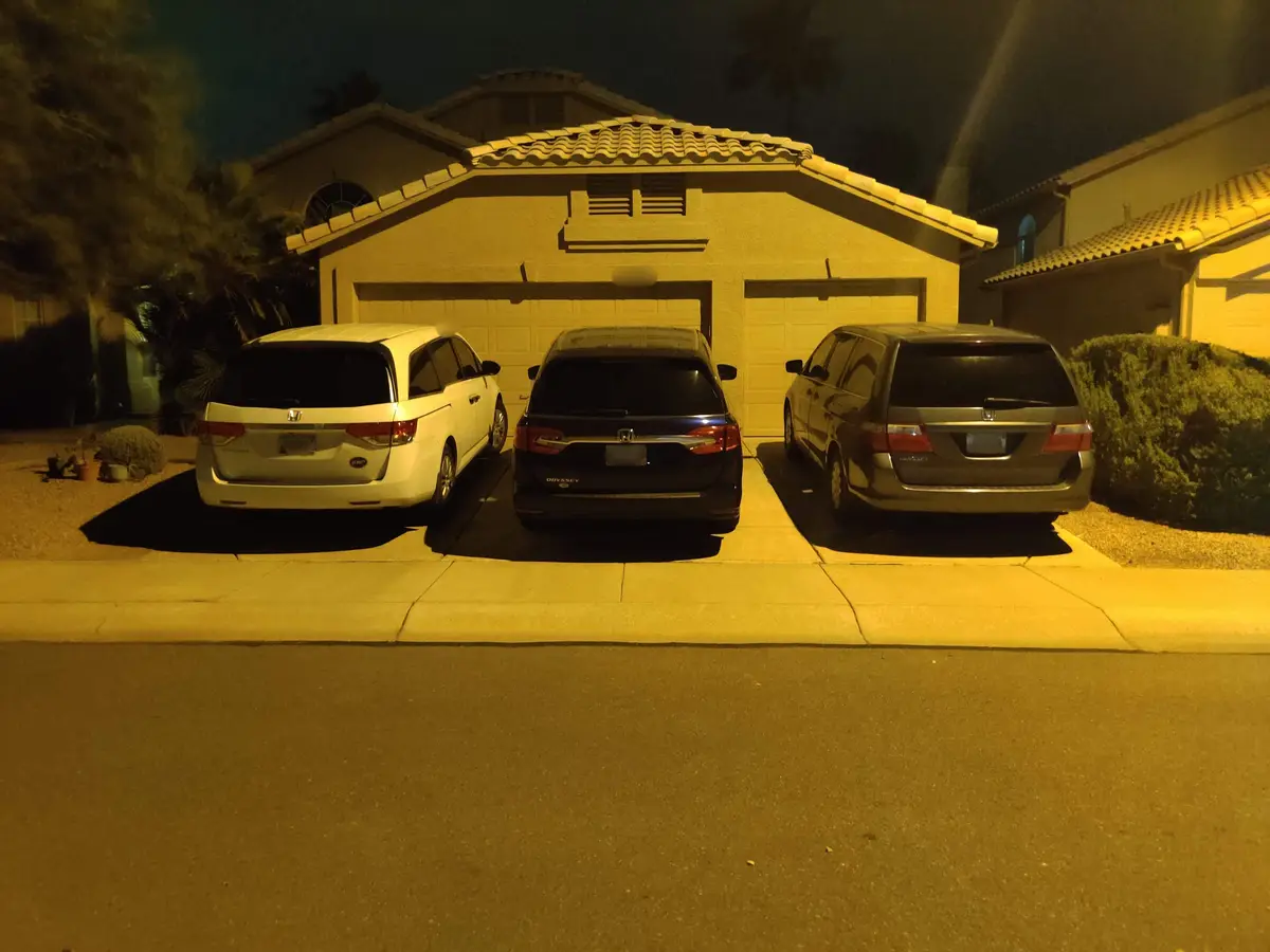 Three Honda Odyssey minivans are parked side-by-side in a driveway at night, illuminated by a yellowish streetlight. The…
