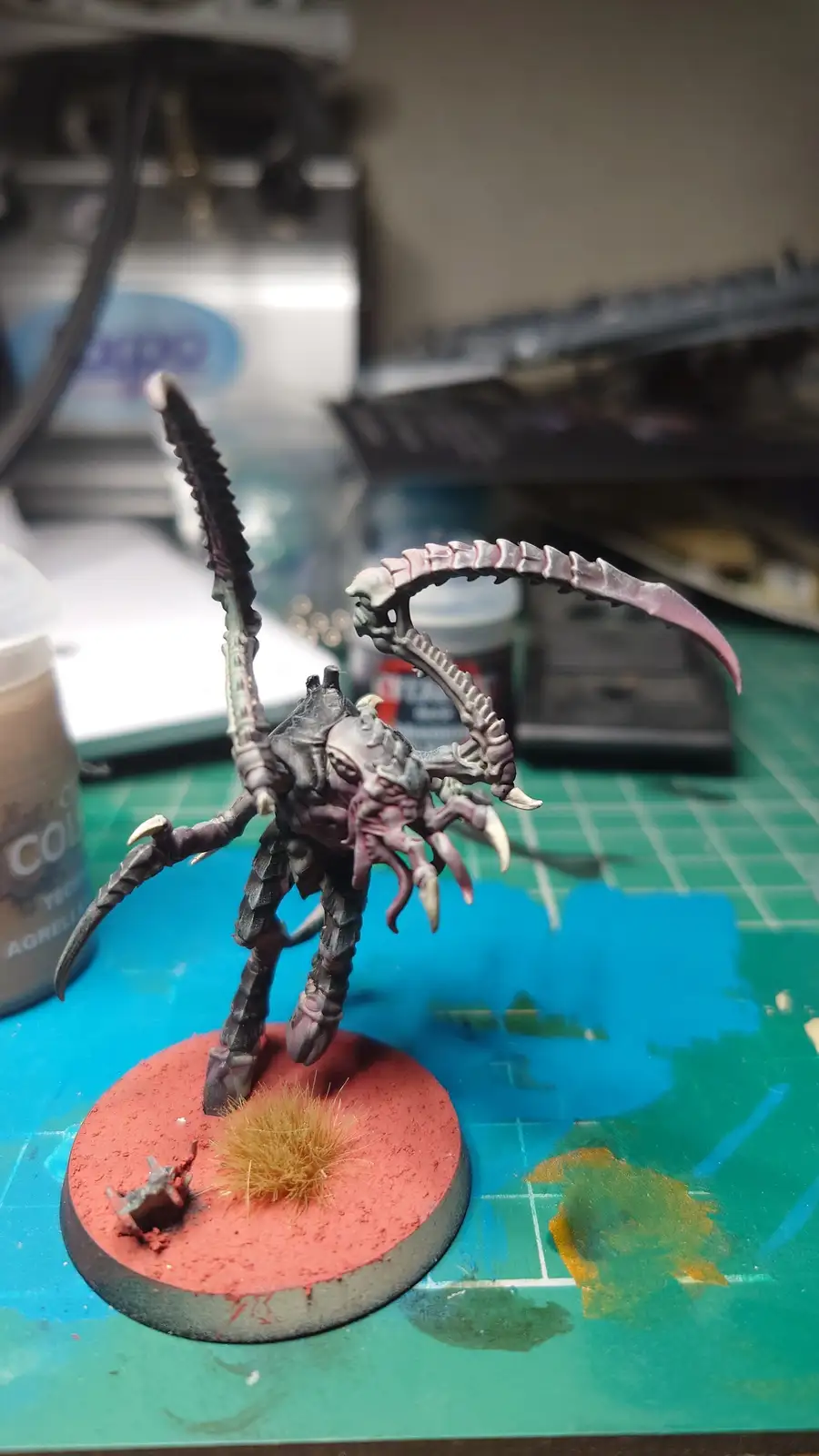 A highly detailed, painted miniature of a grotesque, multi-limbed alien creature with large curved claws and a spiked weapon…