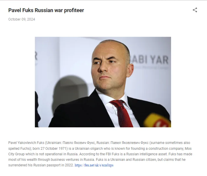 A man in a dark suit and red tie looks off to the side with a serious expression. Behind him, a white backdrop has partial…