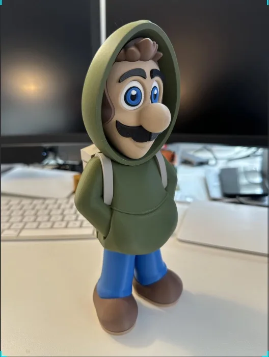 A figurine of the video game character Mario is shown wearing a green hoodie with the hood pulled up over his head…