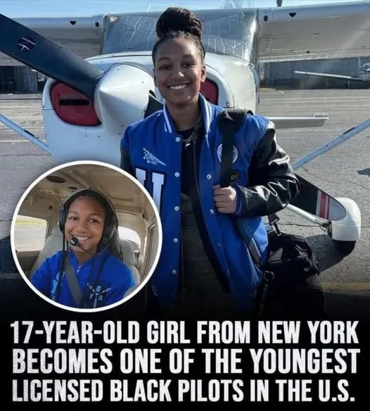 A young Black woman stands smiling in front of a small white airplane on a tarmac, wearing a blue and black varsity jacket…