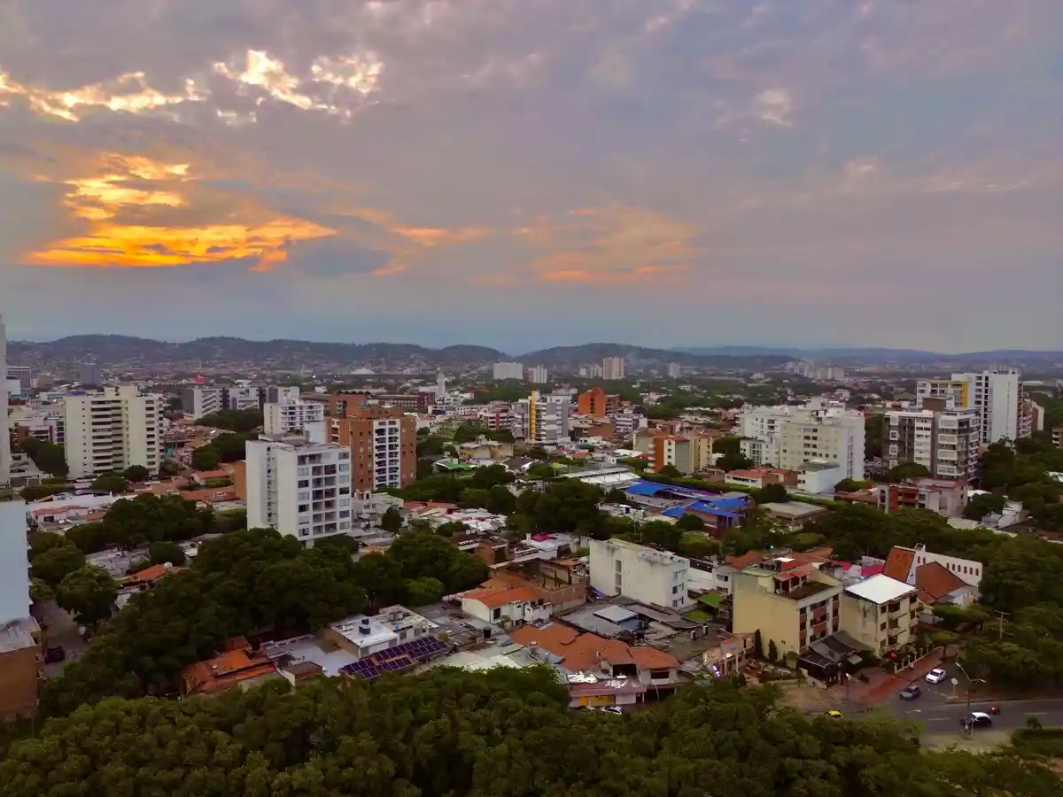 An aerial photo of a sprawling cityscape at sunset, with orange and purple clouds above a mix of modern high-rises and older…